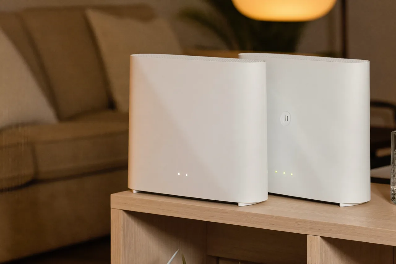 Dois roteadores Wi-Fi brancos lado a lado sobre um móvel de madeira